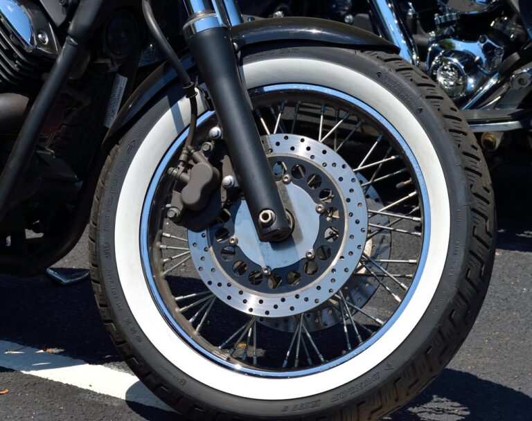 Motocyklista dotykający bieżnika opony tylnego koła motocykla sportowo-turystycznego, sprawdzający jej zużycie i stan techniczny przed wyruszeniem w trasę.