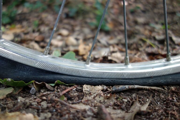 Rowerzysta sprawdzający stan opony rowerowej. Na zbliżeniu widoczny jest starty bieżnik i drobne pęknięcia na bocznej ściance zużytej opony.